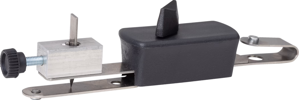 Close-up studio photograph of a small metal clamp-like tool attachment on a white background. The device features a flat stainless-steel mounting plate with a curved end bracket, a black rectangular plastic housing with a short triangular plastic projection on top, and an adjustable aluminum block secured by a threaded steel screw with a black knurled plastic knob. A thin downward-pointing steel blade or cutting tip is visible beneath the aluminum block. The parts show brushed metal and matte plastic surfaces, visible screws and fasteners, and compact, utilitarian construction.